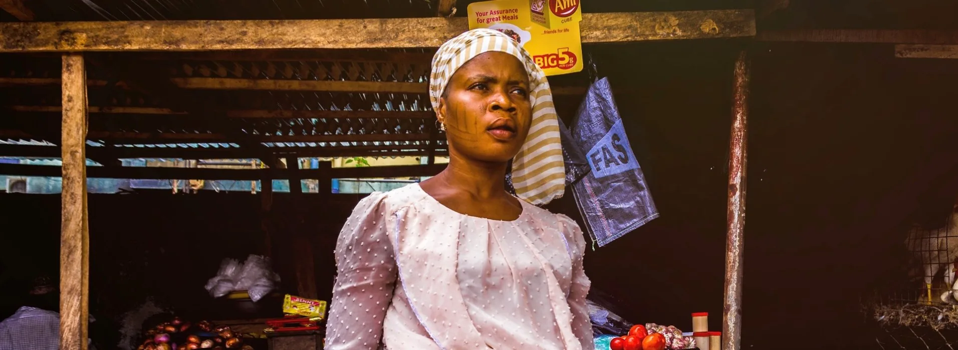 A market trader standing at her stall behind trays of tomatoes, peppers and onions