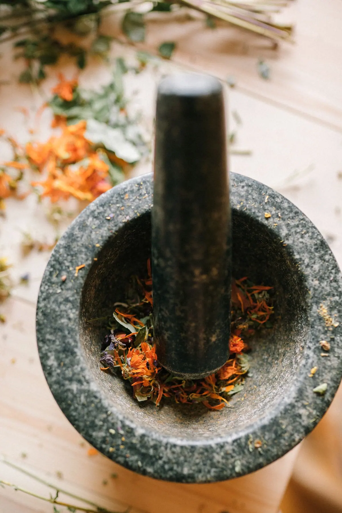 Dried medicinal herbs and flowers ground in a stone mortar and pestle