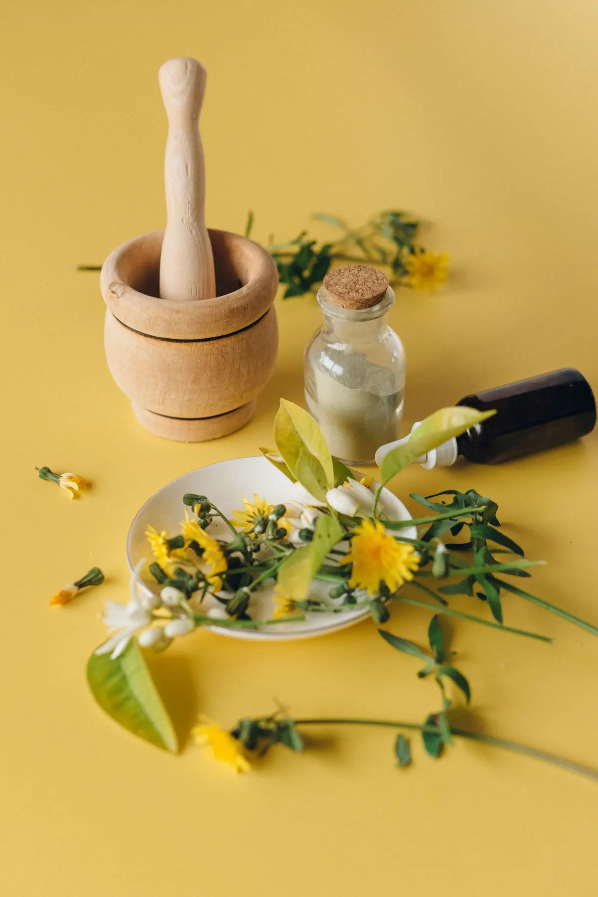 Wooden mortar and pestle, apothecary bottles and fresh flowers laid out for natural remedies