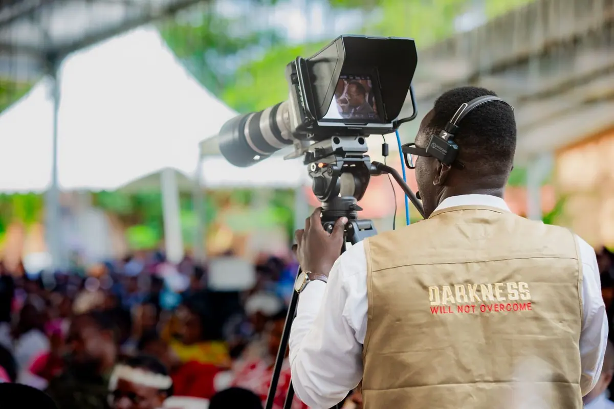 An African cameraman filming a large crowd at an outdoor event