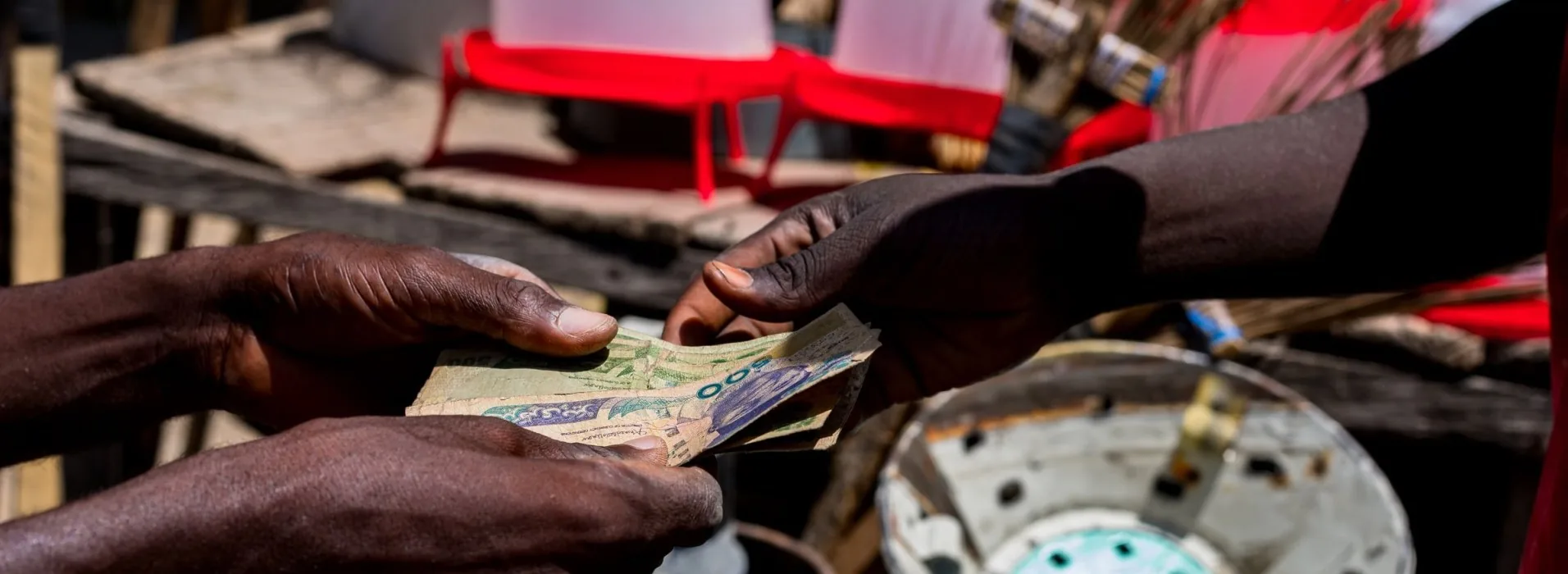 Two pairs of hands exchanging a fold of Nigerian naira notes across a stall at an outdoor market
